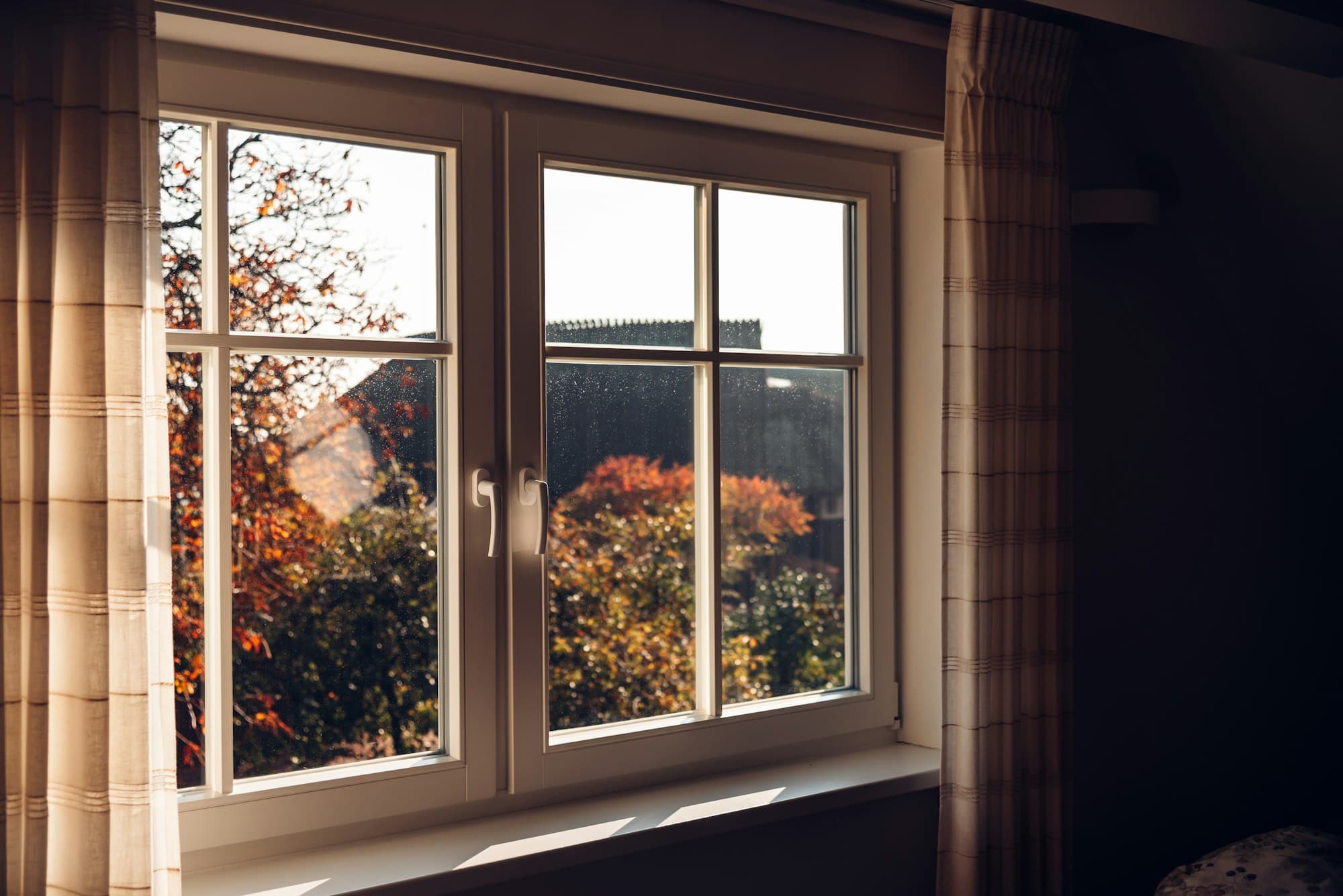 Wit kozijn met helder glas en uitzicht op herfstbomen